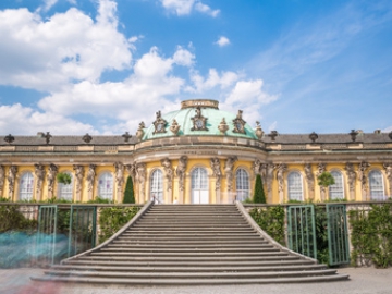 Das Schloss Sanssouci mit seiner großen Freitreppe vor einem blauen Sommerhimmel